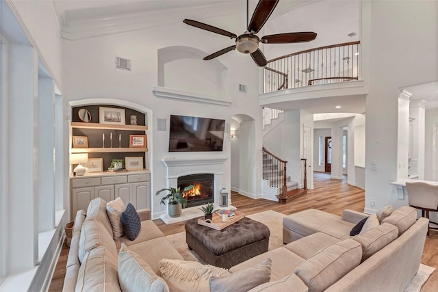 3806 W Benders Landing Blvd, Spring, TX 77386 - living area featuring ceiling fan, wood finished floors, a warm lit fireplace, stairs, and a towering ceiling
