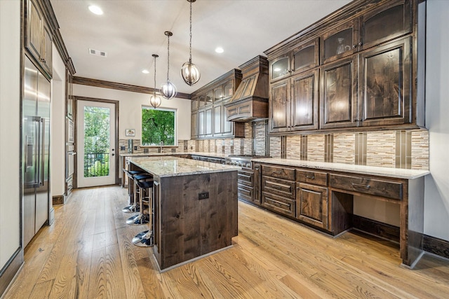 6619 Minola St, Houston, TX 77007 - kitchen with custom exhaust hood, dark brown cabinetry, light wood-type flooring, a kitchen bar, and crown molding