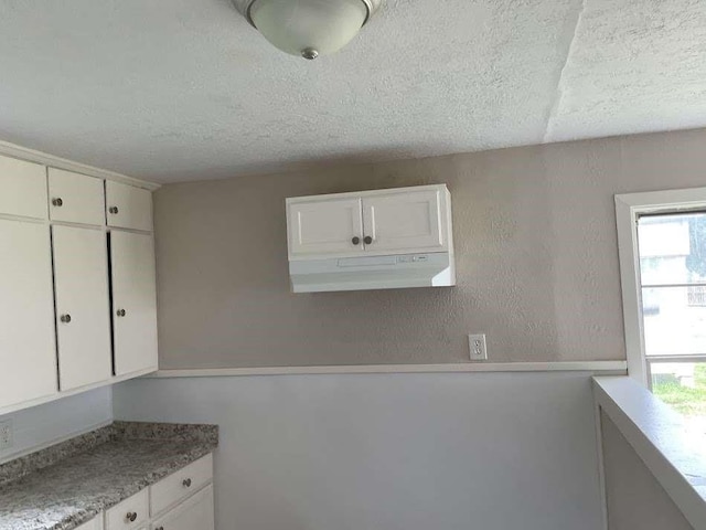 805 E Calhoun St, El Campo, TX 77437 - kitchen with a textured ceiling, white cabinetry, light countertops, and under cabinet range hood