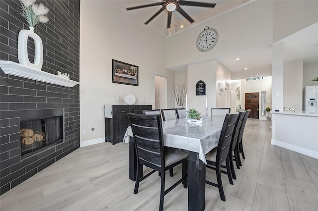 9303 Filaree Ridge Ln, Houston, TX 77089 - dining area featuring a ceiling fan, a towering ceiling, baseboards, light wood-style floors, and a fireplace
