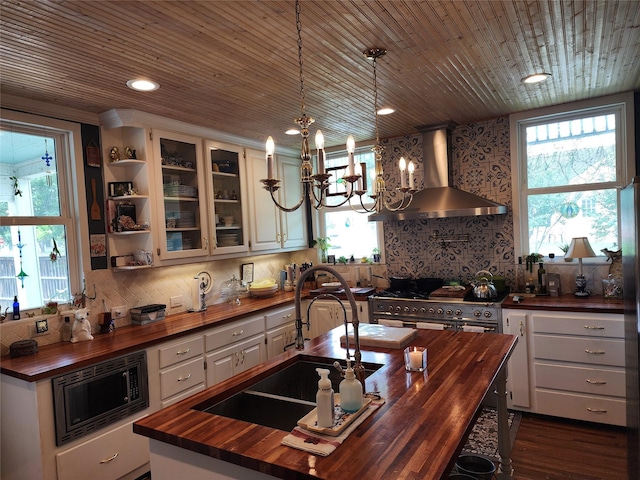 1017 Water St, Navasota, TX 77868 - kitchen with butcher block counters, wall chimney range hood, appliances with stainless steel finishes, a sink, and an island with sink