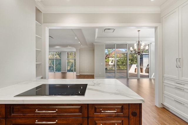 511 S Post Oak Ln Unit 2B, Houston, TX 77056 - kitchen with black electric stovetop, light stone counters, light wood-type flooring, ornamental molding, and a chandelier
