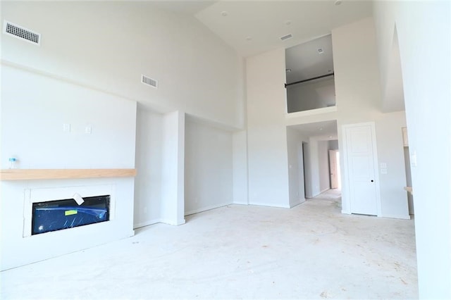 2296 Vargas St, Magnolia, TX 77316 - unfurnished living room featuring a towering ceiling, a glass covered fireplace, concrete floors, and baseboards