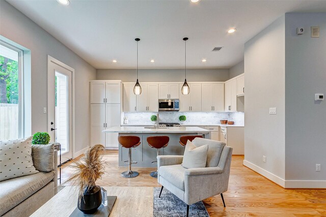 1830 W Tidwell Rd, Houston, TX 77091 - kitchen featuring stainless steel microwave, white cabinets, tasteful backsplash, light wood-type flooring, and a center island with sink