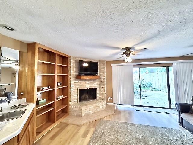 3823 Knollcrest Dr, Montgomery, TX 77356 - unfurnished living room with a sink, light wood-style floors, a fireplace, ceiling fan, and a textured ceiling