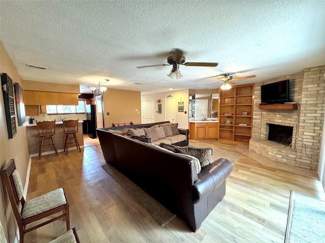 3823 Knollcrest Dr, Montgomery, TX 77356 - living room featuring a textured ceiling, a ceiling fan, light wood-style flooring, a brick fireplace, and built in shelves