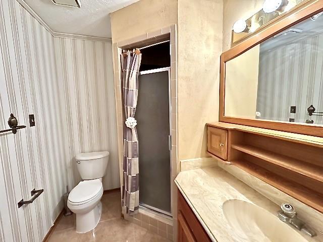 3823 Knollcrest Dr, Montgomery, TX 77356 - full bath featuring toilet, a stall shower, vanity, tile patterned flooring, and wallpapered walls