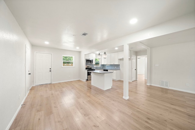 5607 Flamingo Dr, Houston, TX 77033 - kitchen featuring stainless steel appliances, white cabinets, a center island, open floor plan, and light wood finished floors