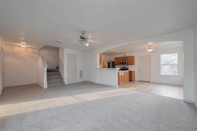 13697 Bighorn Trl, Willis, TX 77378 - unfurnished living room featuring light colored carpet, ceiling fan, baseboards, stairs, and arched walkways