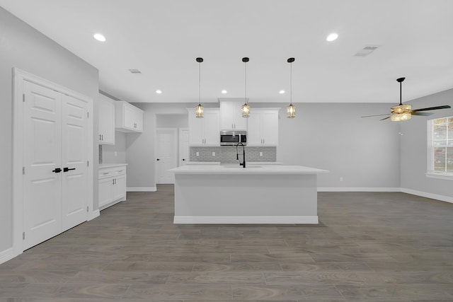 2506 Myrtle St, Waller, TX 77484 - kitchen featuring stainless steel microwave, baseboards, a ceiling fan, tasteful backsplash, and white cabinetry