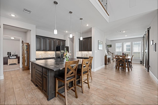 13630 E Palomino Lake Cir, Cypress, TX 77429 - kitchen featuring fridge with ice dispenser, dark countertops, light wood-type flooring, a kitchen island with sink, and decorative backsplash