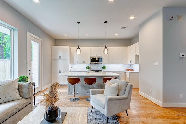 1824 W Tidwell Rd, Houston, TX 77091 - kitchen featuring stainless steel microwave, white cabinets, tasteful backsplash, light wood-style floors, and a kitchen island with sink
