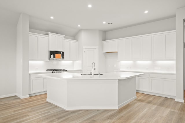 319 Riesling Dr, Alvin, TX 77511 - kitchen with a sink, stainless steel microwave, an island with sink, tasteful backsplash, and light wood finished floors