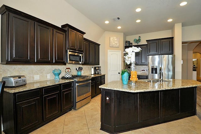 22419 Slate Oaks Ln, Richmond, TX 77469 - kitchen with appliances with stainless steel finishes, arched walkways, backsplash, an island with sink, and light stone counters