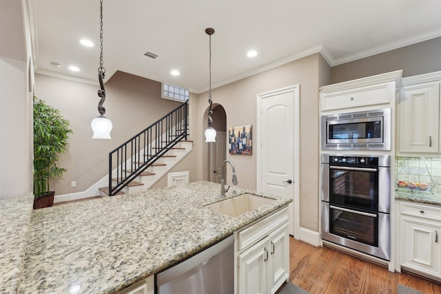 1215 Malone St, Houston, TX 77007 - kitchen featuring appliances with stainless steel finishes, a sink, light wood-style flooring, crown molding, and white cabinets