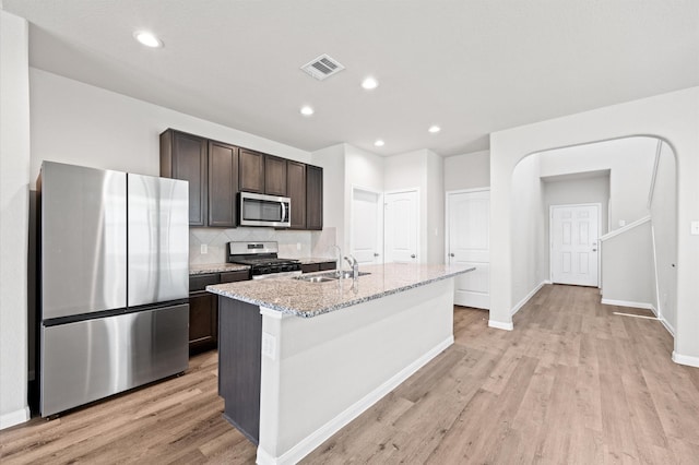 14008 Paddlefish Dr, Conroe, TX 77384 - kitchen with appliances with stainless steel finishes, light wood-type flooring, dark brown cabinetry, a center island with sink, and recessed lighting