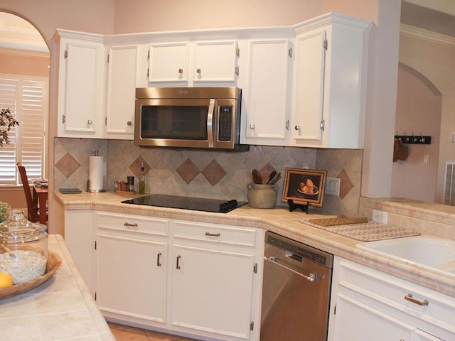 2862 Dees Cir, Sealy, TX 77474 - kitchen with appliances with stainless steel finishes, arched walkways, white cabinetry, decorative backsplash, and ornamental molding