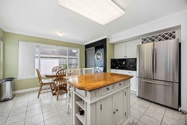 16019 Juniper Grove Dr, Houston, TX 77084 - kitchen featuring freestanding refrigerator, stacked washer and clothes dryer, ornamental molding, white cabinets, and light tile patterned floors