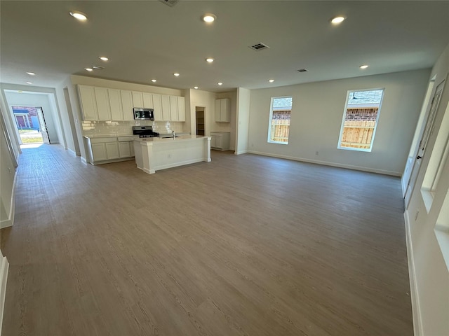 1303 Garrett Sudhendrio Dr, Crosby, TX 77532 - kitchen featuring stainless steel appliances, open floor plan, a kitchen island with sink, backsplash, and white cabinetry