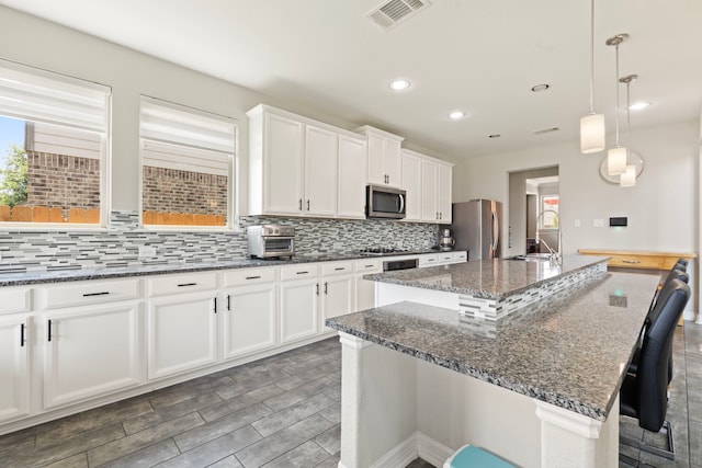 9414 Peralta Creek Ct, Cypress, TX 77433 - kitchen featuring stainless steel appliances, decorative backsplash, a kitchen island with sink, dark stone countertops, and a breakfast bar