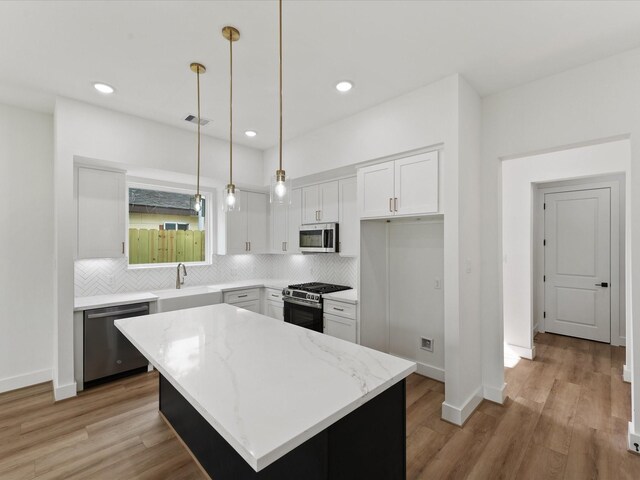 7729 Ave J Unit A, Houston, TX 77012 - kitchen featuring stainless steel appliances, a sink, tasteful backsplash, white cabinets, and light stone counters