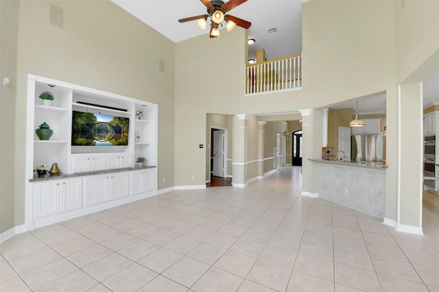 14806 Cantwell Bnd, Cypress, TX 77429 - unfurnished living room with a ceiling fan, a high ceiling, light tile patterned floors, decorative columns, and built in shelves