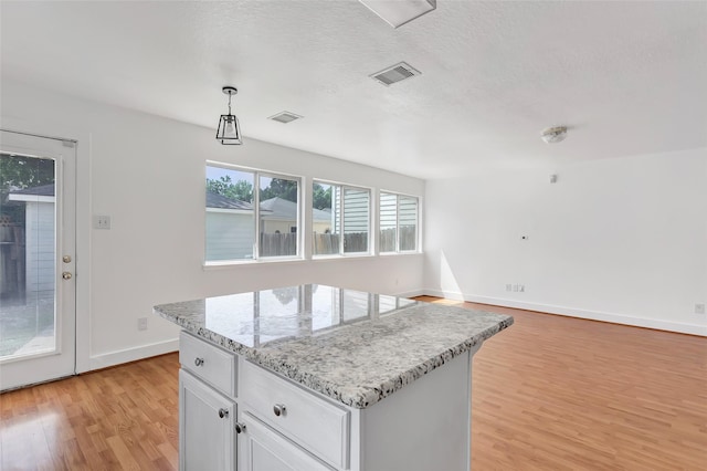 26881 Manor Crest Ct, Kingwood, TX 77339 - kitchen featuring light wood-style floors, a center island, baseboards, white cabinets, and light stone counters