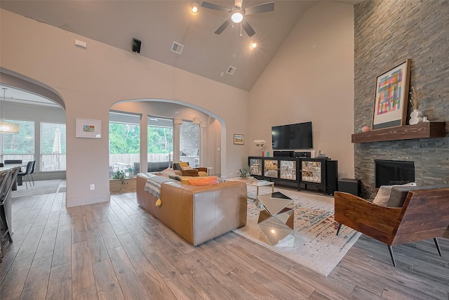 13707 Rivendell Crest Ln, Cypress, TX 77429 - living room with high vaulted ceiling, wood finished floors, a ceiling fan, arched walkways, and a stone fireplace