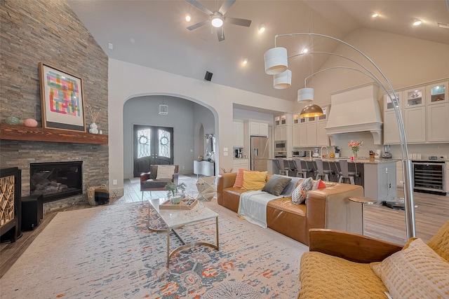 13707 Rivendell Crest Ln, Cypress, TX 77429 - living room with wine cooler, high vaulted ceiling, a ceiling fan, arched walkways, and a stone fireplace
