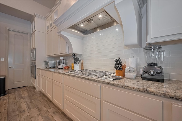13707 Rivendell Crest Ln, Cypress, TX 77429 - kitchen featuring appliances with stainless steel finishes, wall chimney exhaust hood, wood finished floors, glass insert cabinets, and tasteful backsplash
