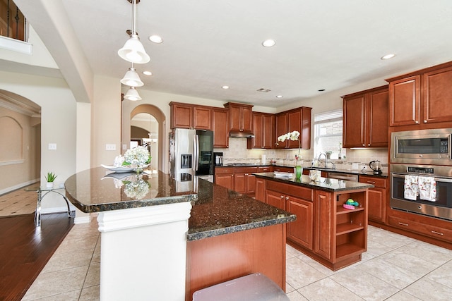 26706 Grey Swan Dr, Katy, TX 77494 - kitchen featuring stainless steel appliances, a center island, arched walkways, open shelves, and backsplash