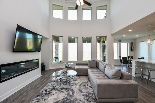 31142 Crescent Hill Dr, Fulshear, TX 77441 - living area with ceiling fan, baseboards, dark wood-style flooring, a towering ceiling, and a glass covered fireplace