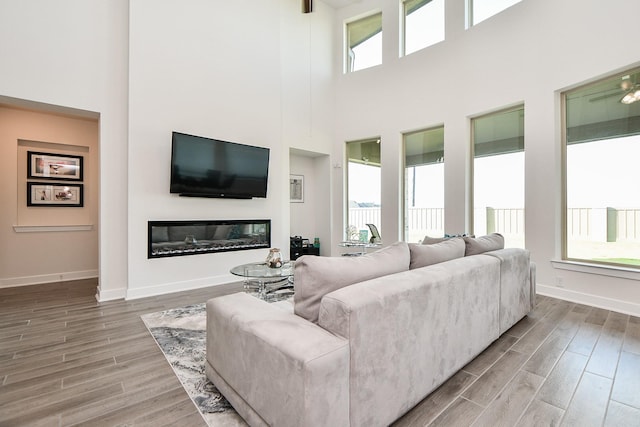 31142 Crescent Hill Dr, Fulshear, TX 77441 - living room featuring light wood-style floors, a high ceiling, a glass covered fireplace, and baseboards