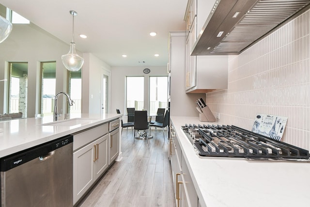 31142 Crescent Hill Dr, Fulshear, TX 77441 - kitchen featuring appliances with stainless steel finishes, extractor fan, a sink, light wood finished floors, and hanging light fixtures