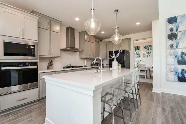 31142 Crescent Hill Dr, Fulshear, TX 77441 - kitchen featuring stainless steel appliances, wall chimney exhaust hood, gray cabinetry, a sink, and light wood-type flooring