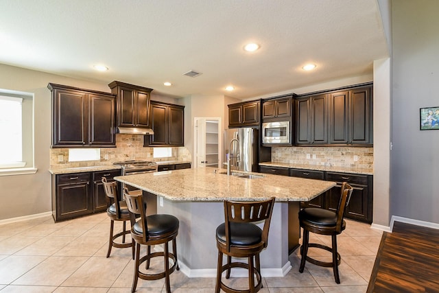 3544 Woods Estates Dr, Conroe, TX 77304 - kitchen with appliances with stainless steel finishes, a sink, under cabinet range hood, light tile patterned floors, and tasteful backsplash