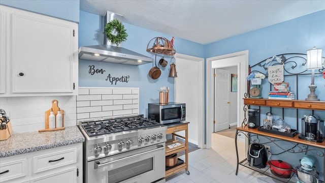 1925 Foxbriar Dr, Huntsville, TX 77340 - kitchen with wall chimney exhaust hood, stainless steel appliances, tasteful backsplash, white cabinets, and light stone counters