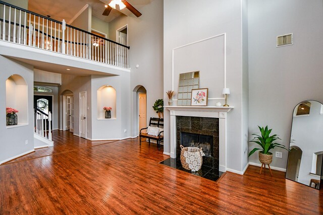 1638 Brookstone Ln, Sugar Land, TX 77479 - living room featuring a high ceiling, a ceiling fan, arched walkways, a tiled fireplace, and wood finished floors