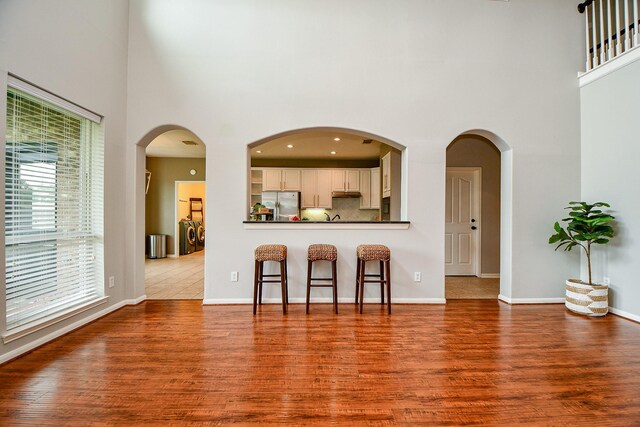 1638 Brookstone Ln, Sugar Land, TX 77479 - kitchen with stainless steel fridge with ice dispenser, a towering ceiling, a kitchen breakfast bar, wood finished floors, and dark countertops