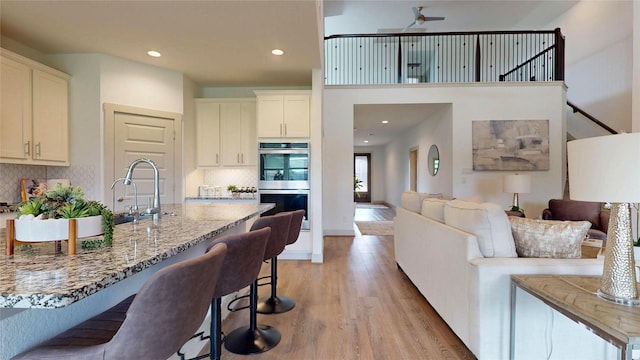 3539 Gore Creek Dr, Katy, TX 77494 - kitchen featuring double oven, light wood finished floors, a kitchen breakfast bar, backsplash, and light stone counters