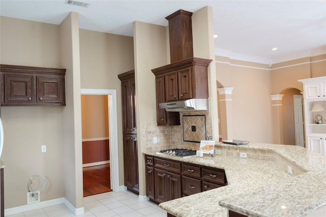 1818 Janell Rene Cir, Deer Park, TX 77536 - kitchen with under cabinet range hood, stainless steel gas cooktop, a peninsula, light tile patterned floors, and arched walkways