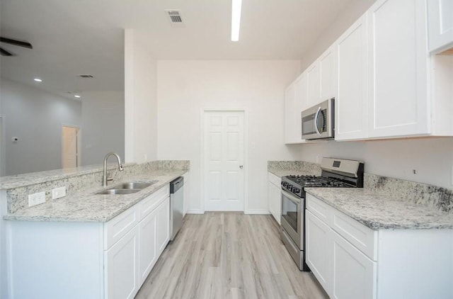 2352 Cedar Place Dr, Conroe, TX 77306 - kitchen with appliances with stainless steel finishes, a sink, a peninsula, light wood-style flooring, and white cabinetry