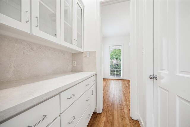 4521 Palmetto St, Bellaire, TX 77401 - kitchen featuring light wood-style flooring, decorative backsplash, glass insert cabinets, white cabinetry, and light stone counters