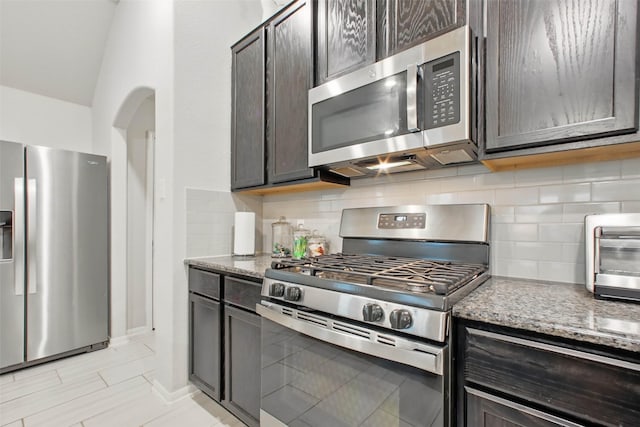 15322 Laceleaf Trl, Houston, TX 77044 - kitchen with stainless steel appliances, decorative backsplash, stone countertops, dark brown cabinets, and arched walkways