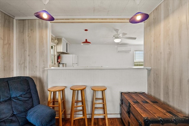 227 Detenbeck Ave, Surfside Beach, TX 77541 - kitchen featuring freestanding refrigerator, ceiling fan, wooden walls, a wall unit AC, and wood finished floors