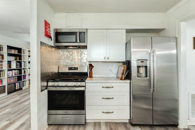 117 Tuna St, Galveston, TX 77550 - kitchen with stainless steel appliances, light wood finished floors, white cabinets, tasteful backsplash, and light stone countertops
