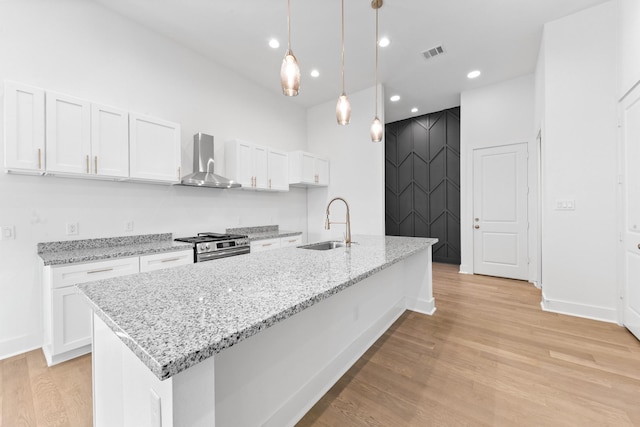 4710 Gunter St, Houston, TX 77020 - kitchen featuring wall chimney exhaust hood, a sink, stainless steel range, light wood-style flooring, and white cabinetry