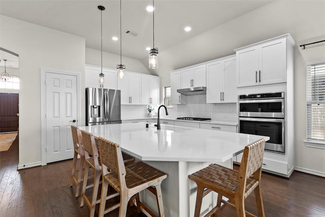 6015 Birchwood Cliff Trl, Katy, TX 77493 - kitchen featuring appliances with stainless steel finishes, decorative backsplash, under cabinet range hood, dark wood finished floors, and light countertops