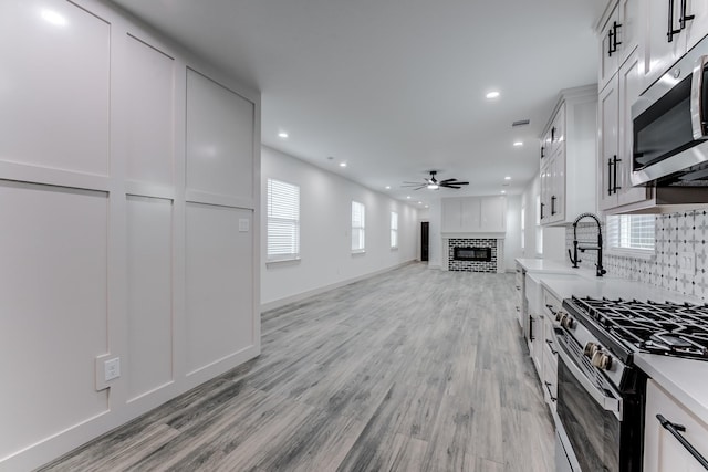 337 Todd St, Tomball, TX 77375 - kitchen with appliances with stainless steel finishes, a ceiling fan, recessed lighting, a glass covered fireplace, and light wood-type flooring