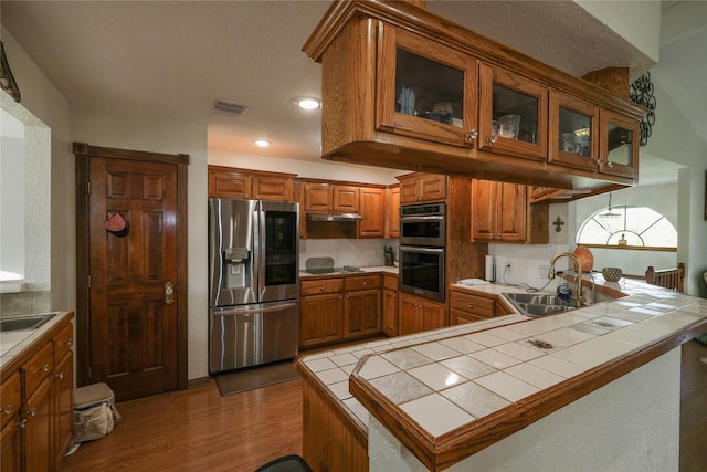 4746 County Road 502d, Sweeny, TX 77480 - kitchen with appliances with stainless steel finishes, tile countertops, brown cabinetry, a sink, and a peninsula